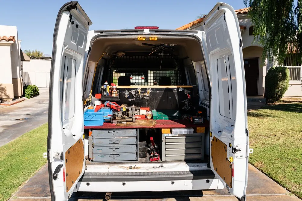 Jeff's white work van seen from behind with both rear doors open, showing the workbench, drawers and tools inside.
