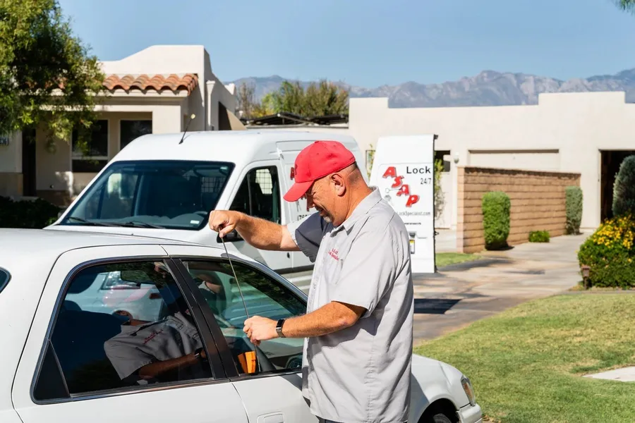 Jeff Slama of ASAP Lock Specialist unlocking the door of a white car, with his work van parked behind him.