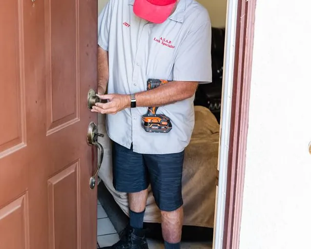 Jeff's hands on the deadbolt of a brown front door, with a cordless drill held against his side.